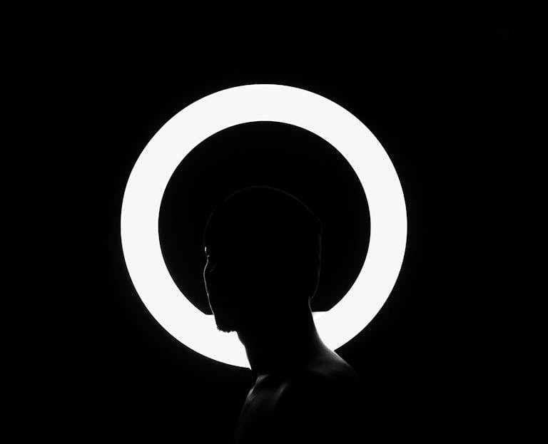 Striking black and white silhouette of a man against a bright circular light background.