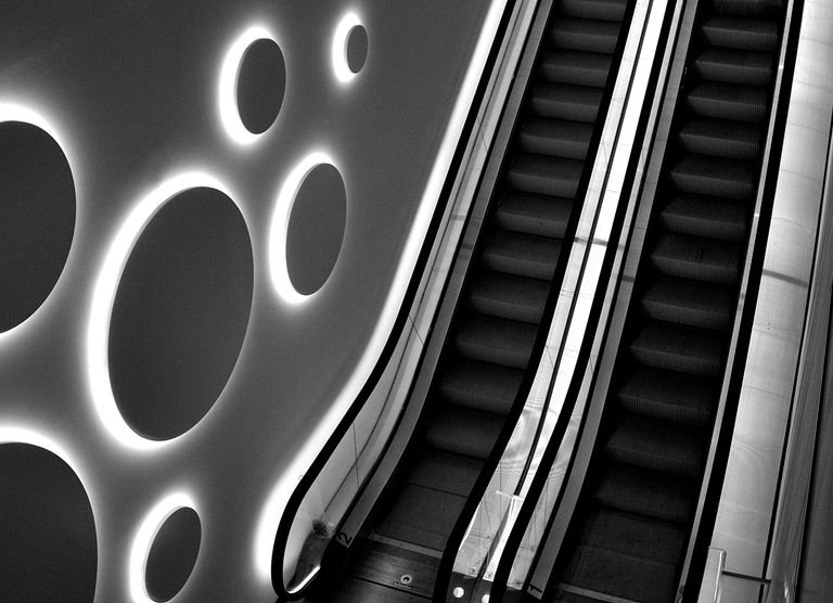 Stylish black and white photo of an escalator with modern circular lighting design.