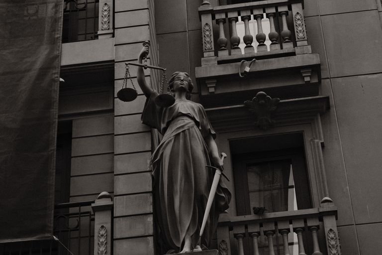 A black and white image of Lady Justice statue against a building facade symbolizing law and fairness.