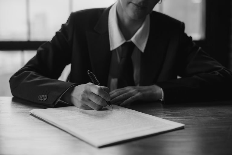 Black and white photo of a businessperson writing on a document indoors.