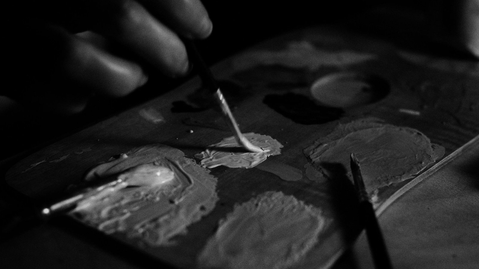Black and white image of an artist mixing paint on a palette using a fine brush.